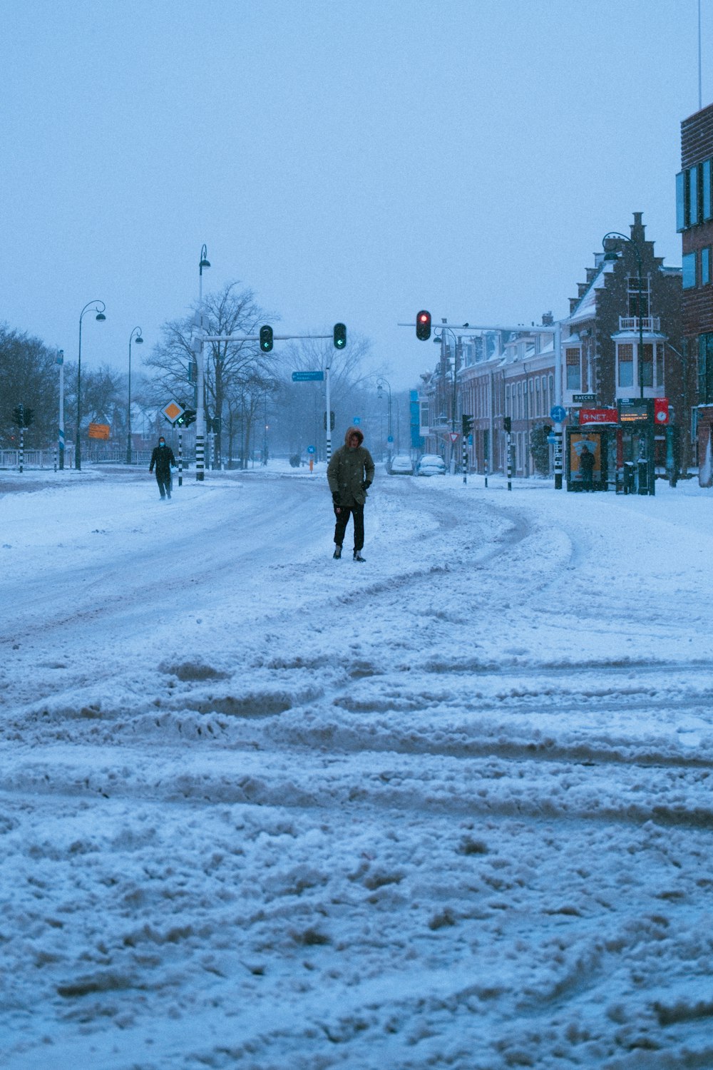 昼間、雪に覆われた道を歩く黒いコートを着た人
