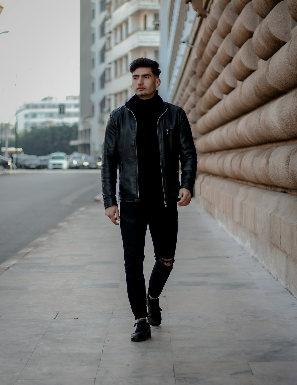 man in black leather jacket standing on sidewalk during daytime