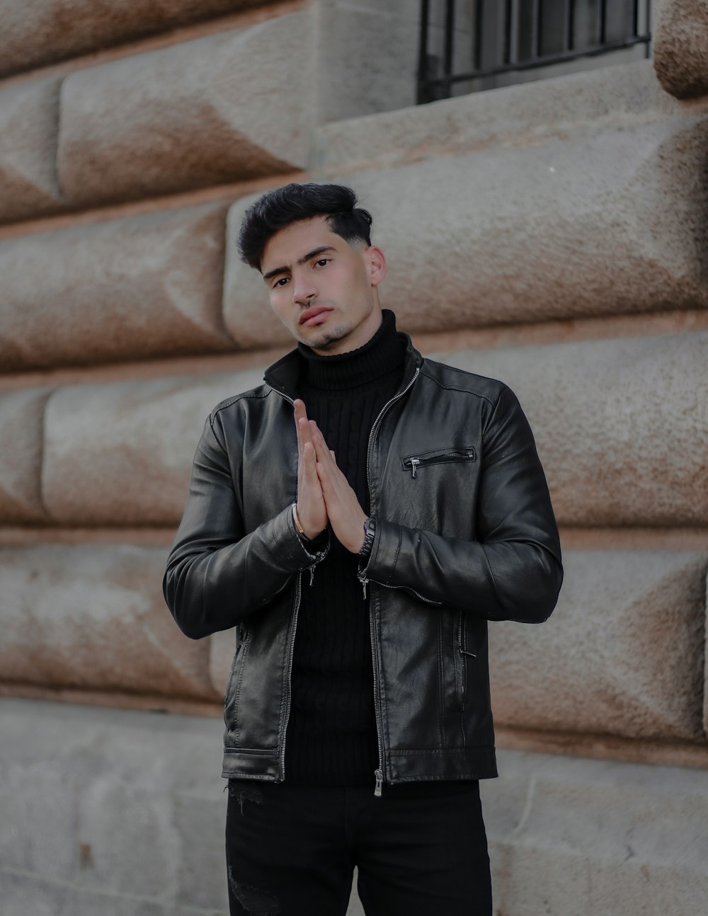 man in black leather jacket standing near brown concrete wall during daytime