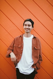 man in brown leather jacket standing beside red wall