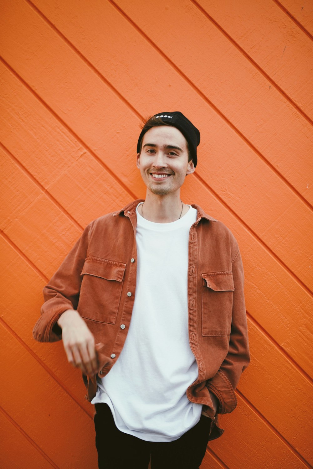 man in brown leather jacket standing beside red wall