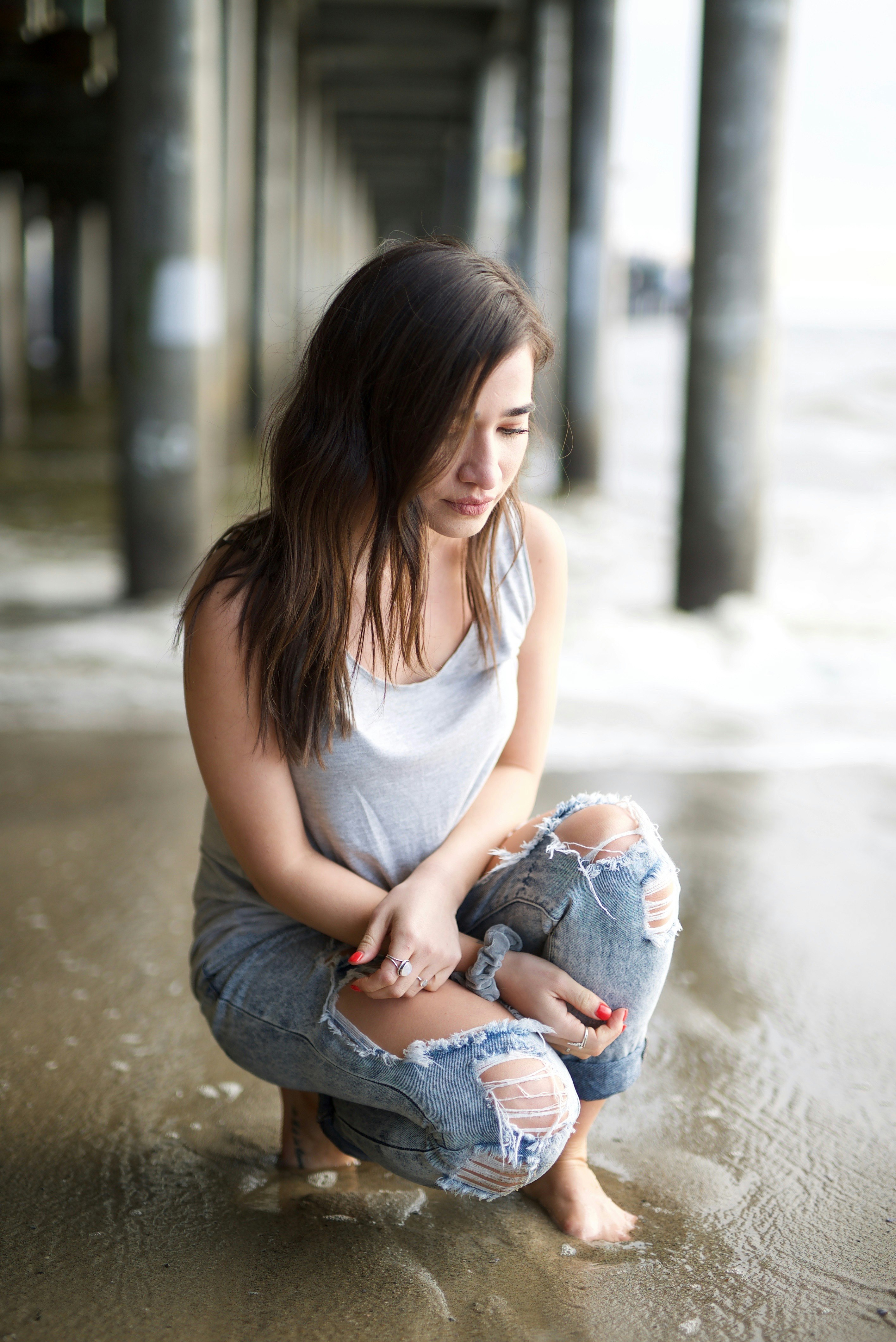 woman in white tank top and blue denim jeans sitting on concrete floor during daytime