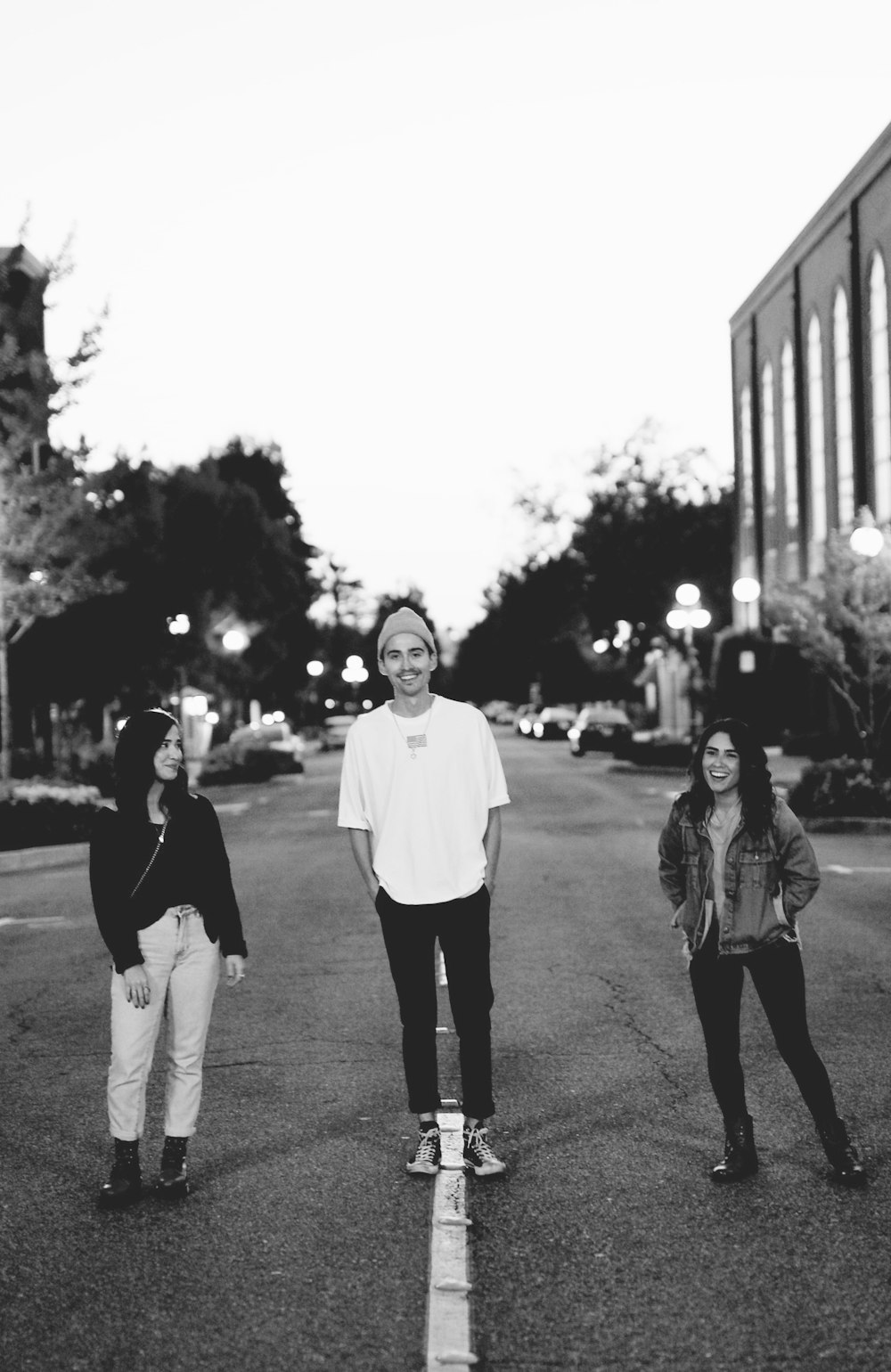 grayscale photo of 2 women and man standing on road