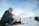 A snowboarder laughing with a Triple Canber strapped to their board, cans visible and snow falling around.