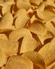 A close-up view of a pile of crispy, golden potato chips with a textured surface, highlighting their curved shape and appetizing appearance.