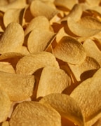 A close-up view of a pile of crispy, golden potato chips with a textured surface, highlighting their curved shape and appetizing appearance.