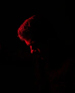 Close-up of a model's silhouette illuminated by soft crimson light in an empty alley.