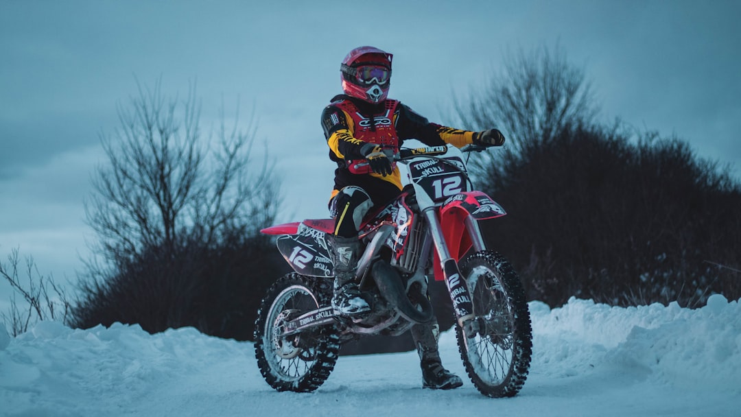 man in black and red jacket riding red and black motorcycle on snow covered ground during