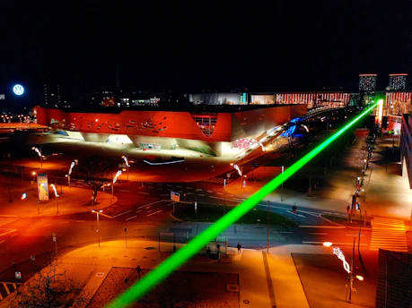 A modern laser scanner in action scanning a complex building and landscape under bright studio lighting.