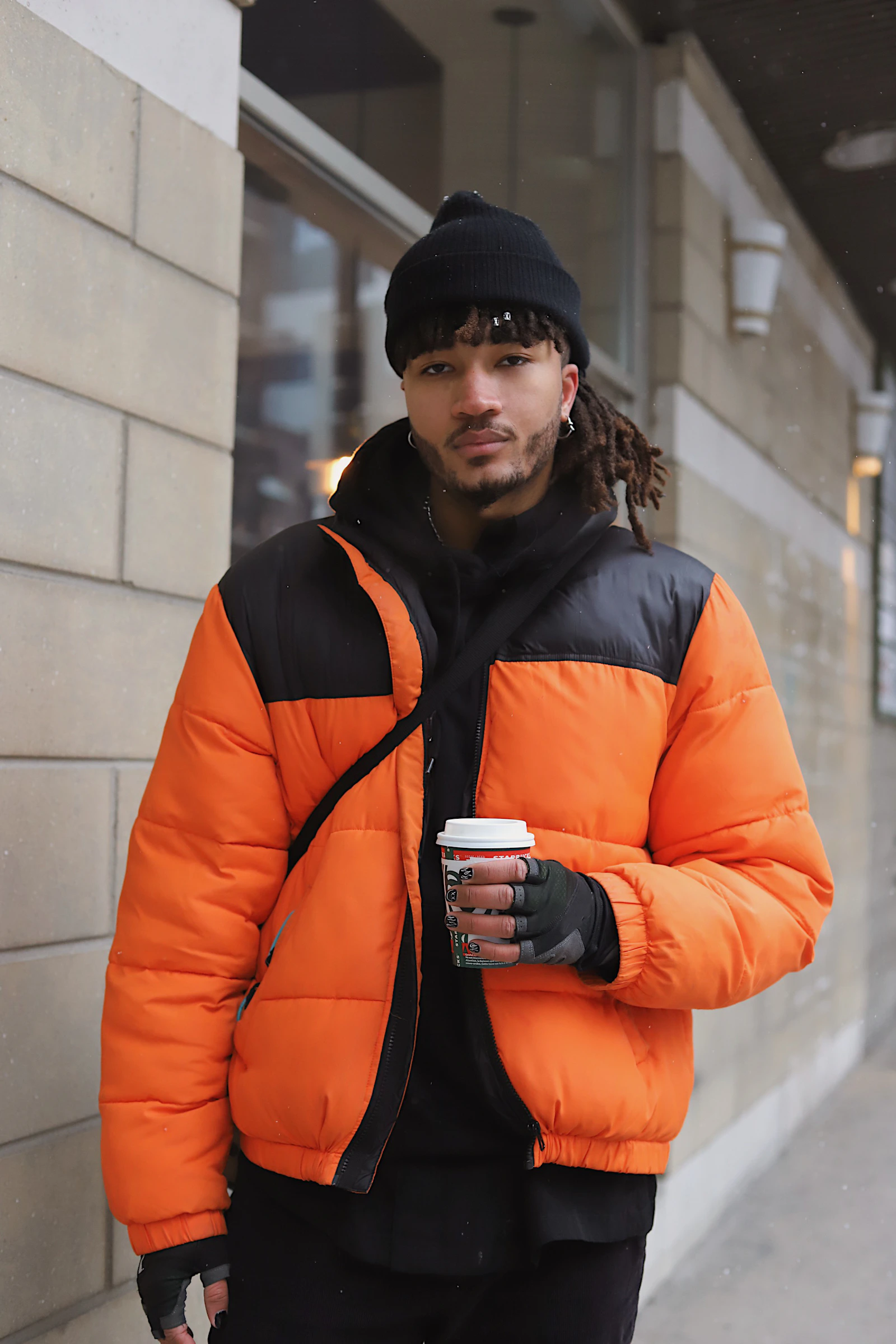 Man in orange and black puffer jacket holding coffee