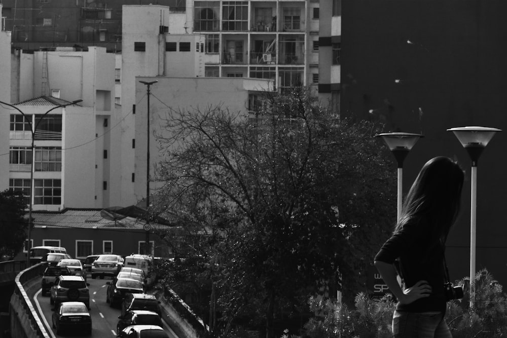 Foto in scala di grigi di uomo in camicia nera e pantaloni in piedi vicino all'edificio