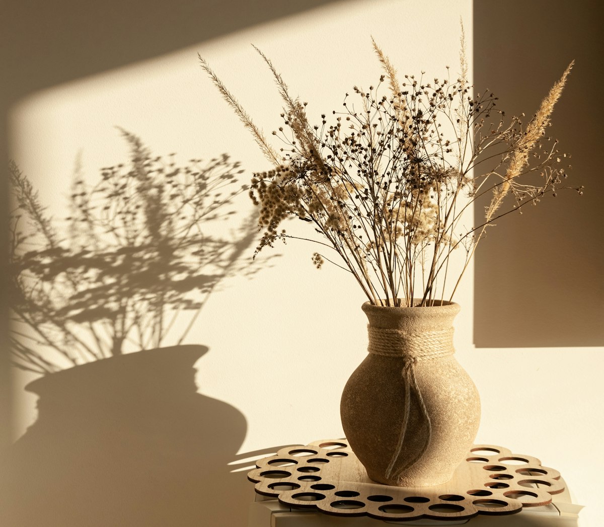 Bouquet de graminées séchées dans un vase en terre cuite exposé au soleil direct, lumière qui décolore les fleurs séchées à terme