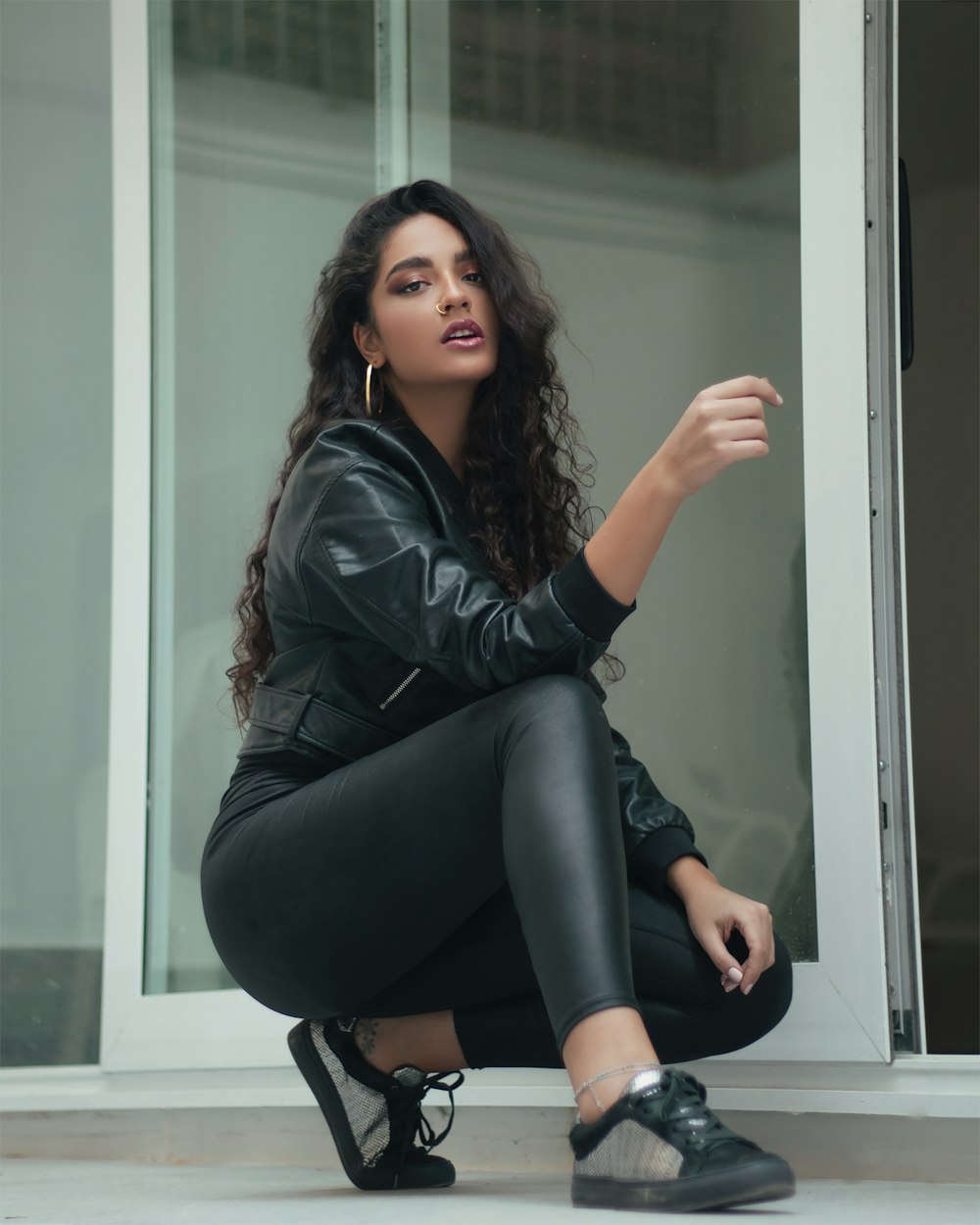 woman in black leather jacket and black leggings sitting on glass window
