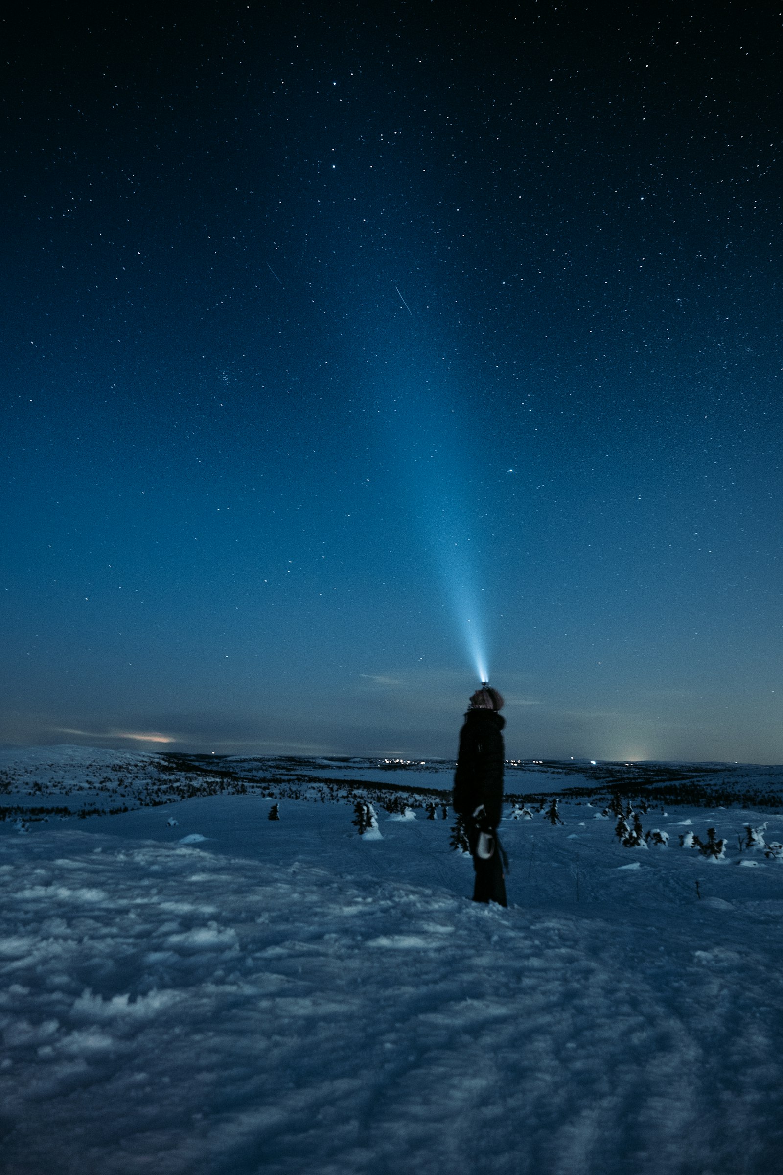 Une personne debout dans la neige, le faisceau de sa lampe frontale dans la nuit