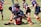 A group of young rugby players are in the midst of a game on a grassy field. They are wearing colorful uniforms, with one team in black and red and the other in blue and red. The players are engaged in a tackle, displaying teamwork and athleticism.