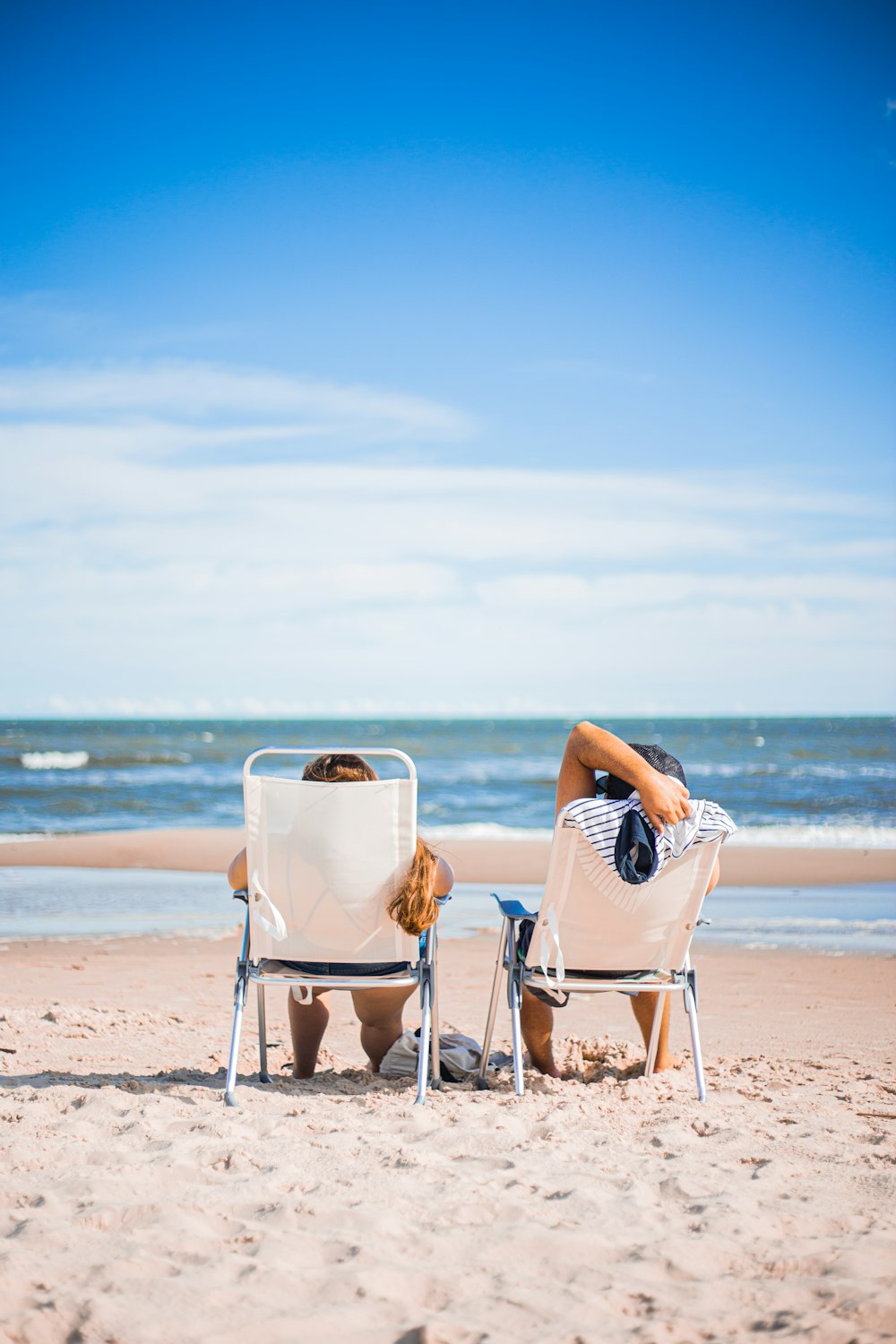 femme en robe rayée noire et blanche assise sur une chaise blanche sur la plage pendant la journée
