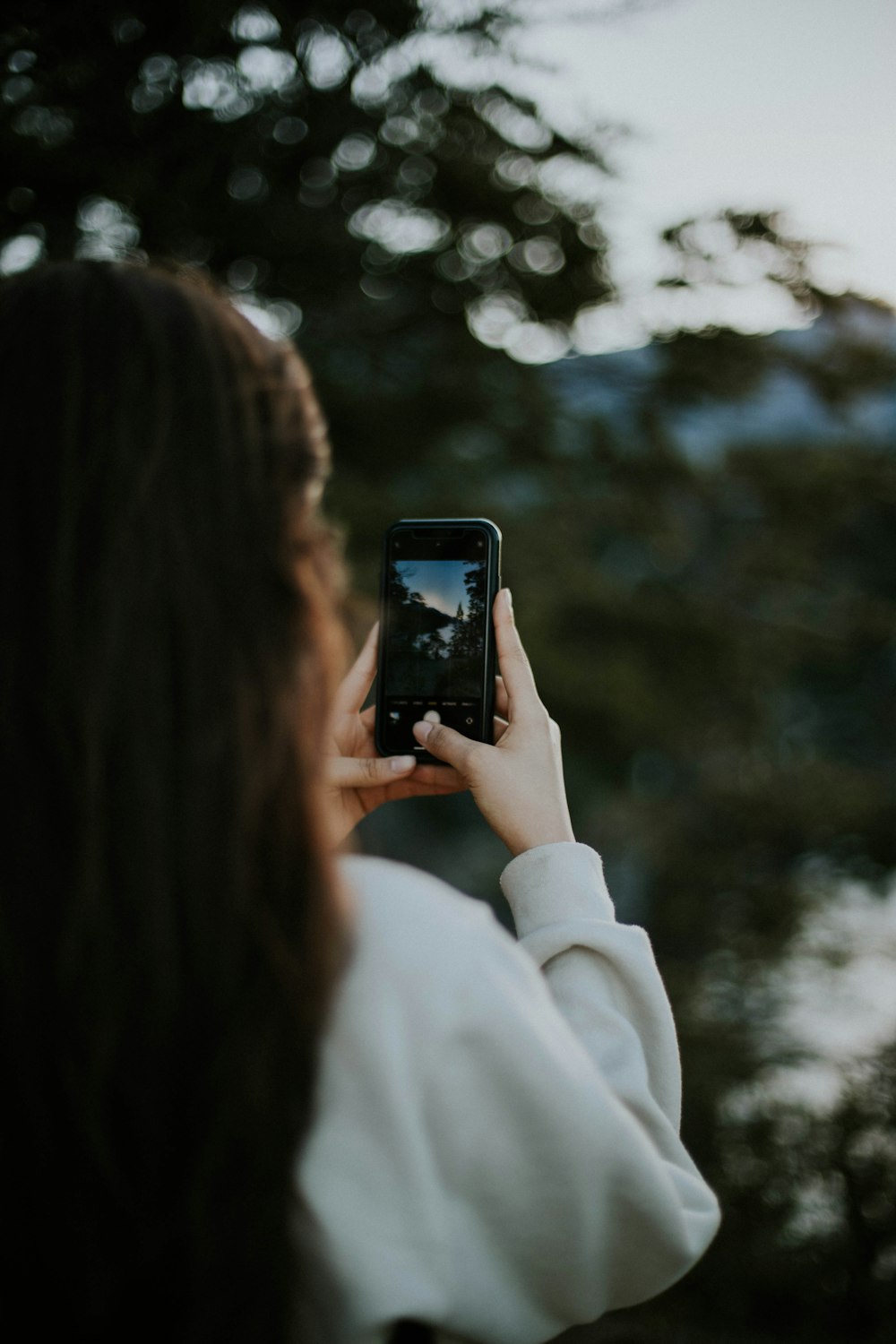 woman in white coat holding black smartphone