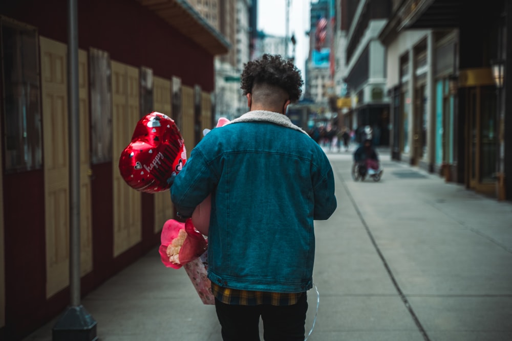 man in blue dress shirt and black pants holding red heart balloon