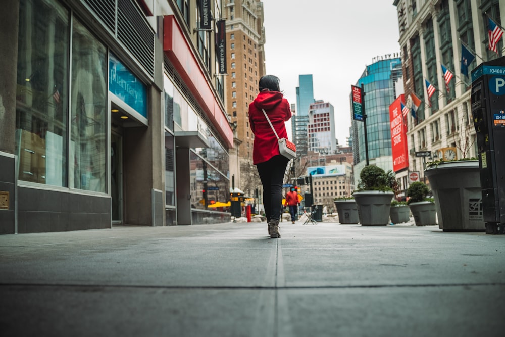 man in red jacket and black pants walking on sidewalk during daytime