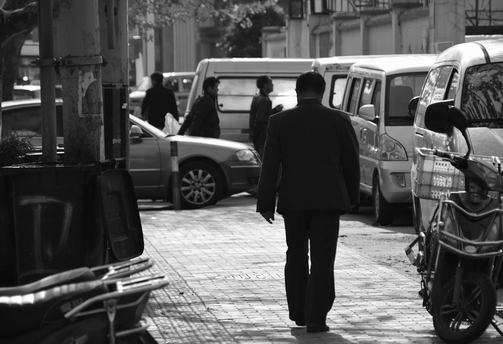man in black coat standing near car in grayscale photography