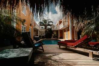 Sunlit courtyard with vibrant tropical plants surrounding a sparkling lap pool beside charming beach-boho apartments.