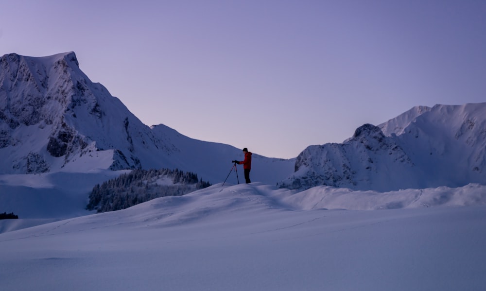 Persona in giacca rossa e pantaloni neri in piedi su terreno coperto di neve durante il giorno