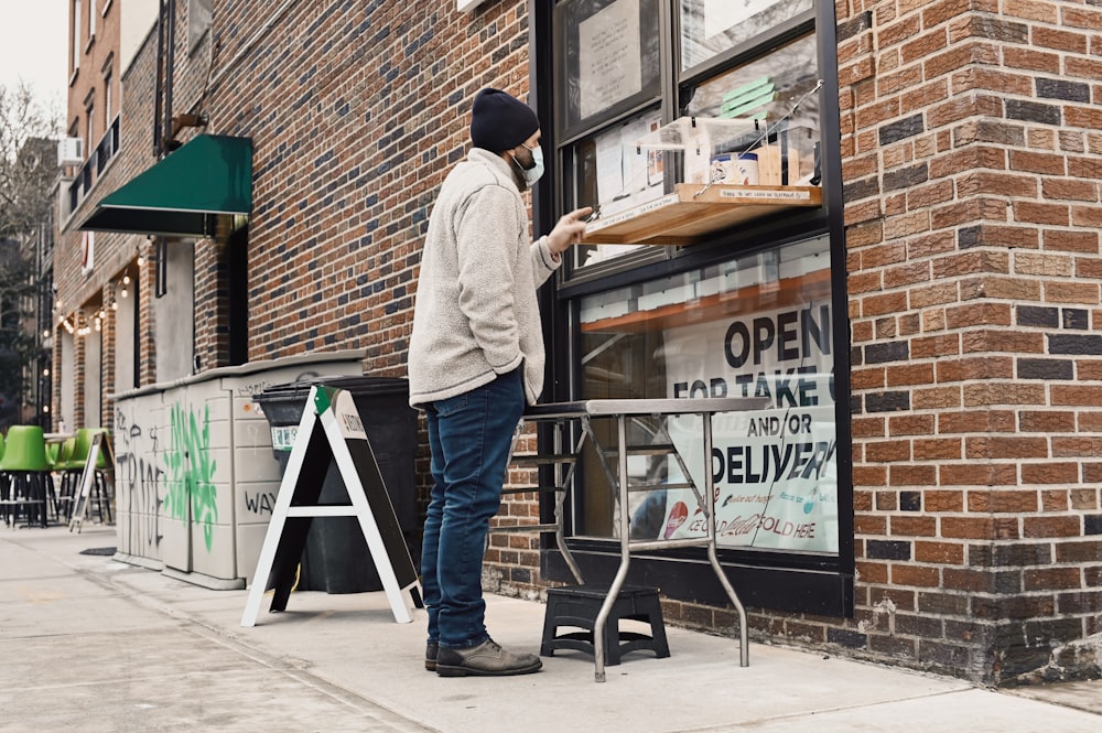 man in white long sleeve shirt and blue denim jeans standing in front of store