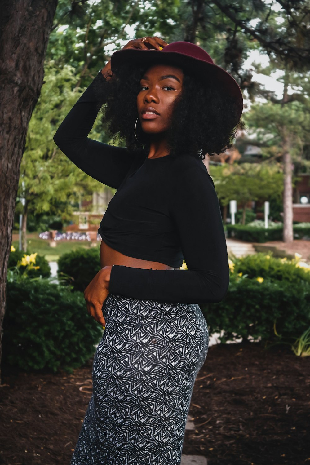 woman in black long sleeve shirt and white and black floral skirt standing near green tree