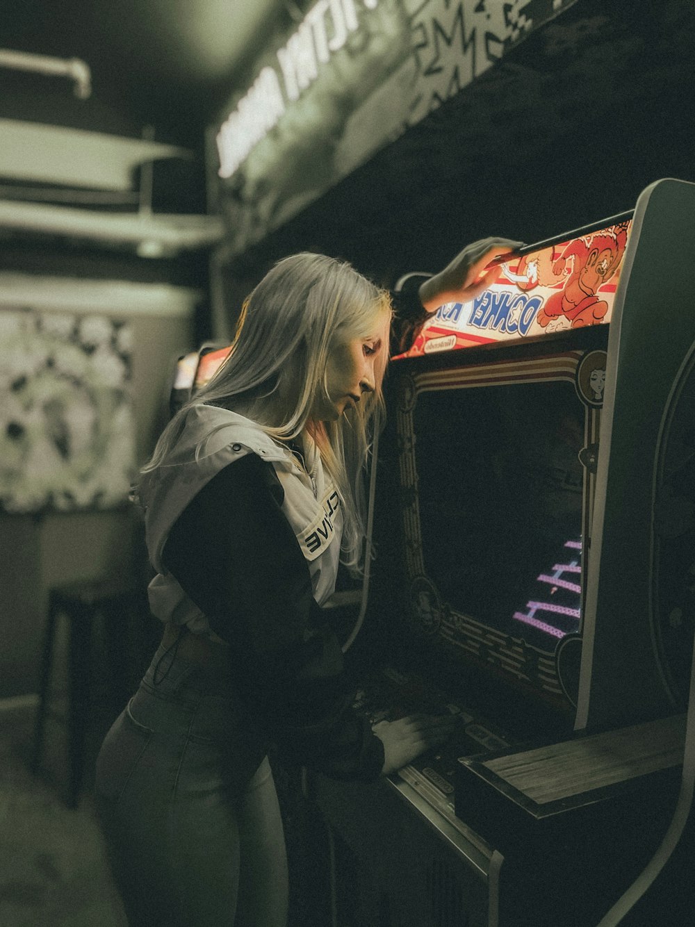 woman in black jacket and blue denim jeans standing in front of arcade machine