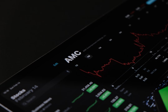 A digital stock trading interface with the focus on AMC Entertainment Holdings, Inc. The screen displays various financial data including stock prices, volume, and market cap. A red line graph shows stock performance over time and several buttons allow for different time frame selections like 1W, 1M, and 1Y. Various stock metrics appear in rows and columns.