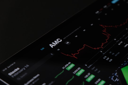A digital stock trading interface with the focus on AMC Entertainment Holdings, Inc. The screen displays various financial data including stock prices, volume, and market cap. A red line graph shows stock performance over time and several buttons allow for different time frame selections like 1W, 1M, and 1Y. Various stock metrics appear in rows and columns.
