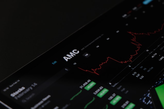 A digital stock trading interface with the focus on AMC Entertainment Holdings, Inc. The screen displays various financial data including stock prices, volume, and market cap. A red line graph shows stock performance over time and several buttons allow for different time frame selections like 1W, 1M, and 1Y. Various stock metrics appear in rows and columns.