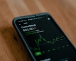 A smartphone displays stock market information, specifically for GameStop, highlighting the current price and a green graph indicating stock fluctuations.