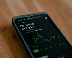 A smartphone displays stock market information, specifically for GameStop, highlighting the current price and a green graph indicating stock fluctuations.