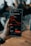 A hand holding a smartphone displaying a stock trading app screen. The app shows stock information for AMC Entertainment, including a line graph of its performance, current price, and trading options.