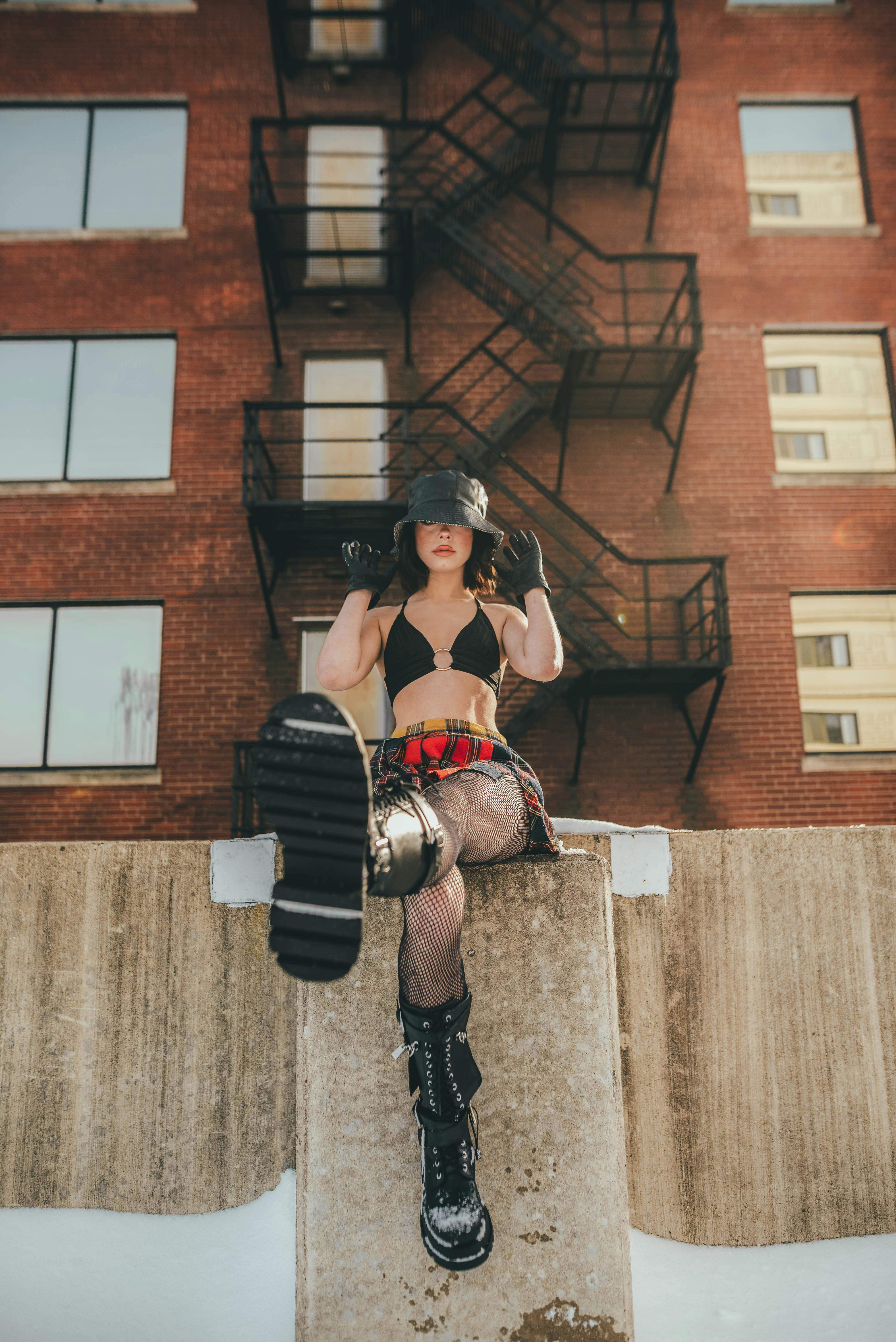 woman in black leather jacket and black pants wearing black gloves standing beside brown brick building