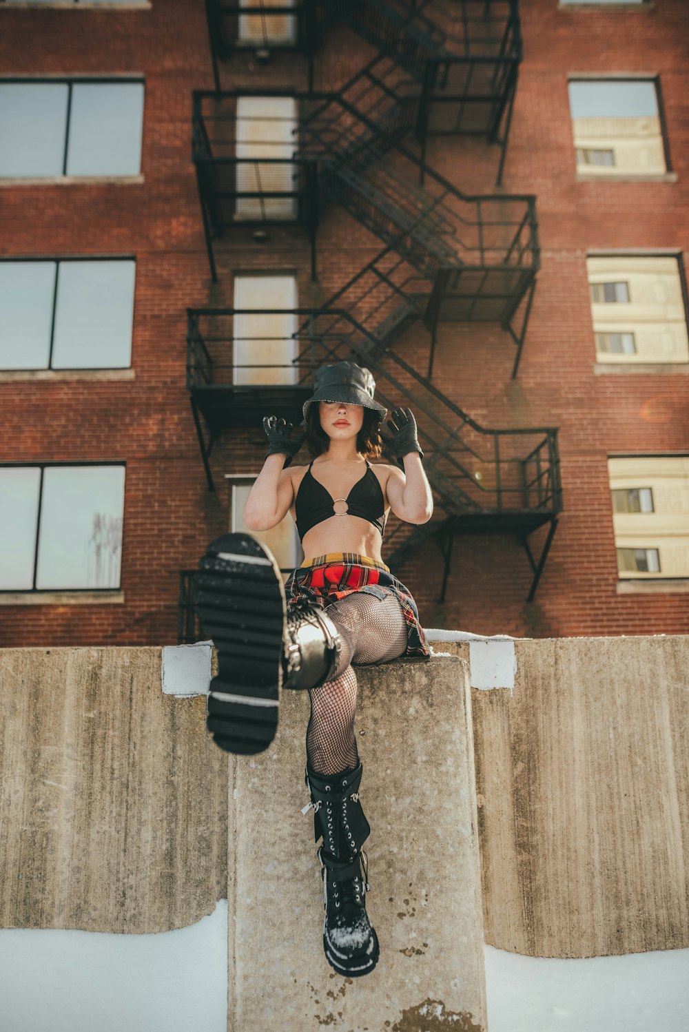 woman in black leather jacket and black pants wearing black gloves standing beside brown brick building