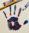 A colorful handprint created with red, blue, and hints of black paint is displayed on a white canvas. Beside the handprint are a wooden-handled paintbrush and tubes of red and blue acrylic paint.