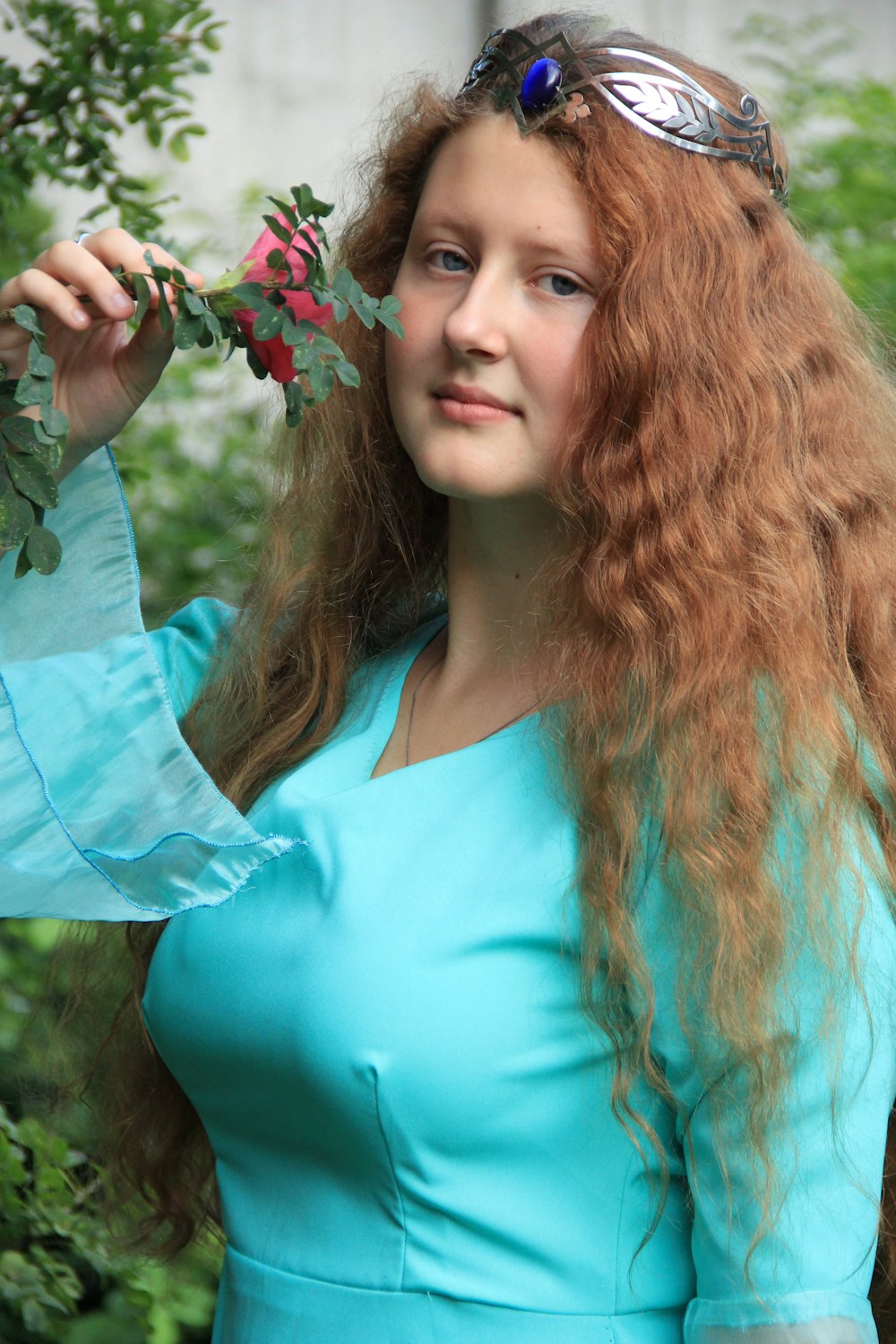 woman in teal scoop neck shirt holding red and white flower