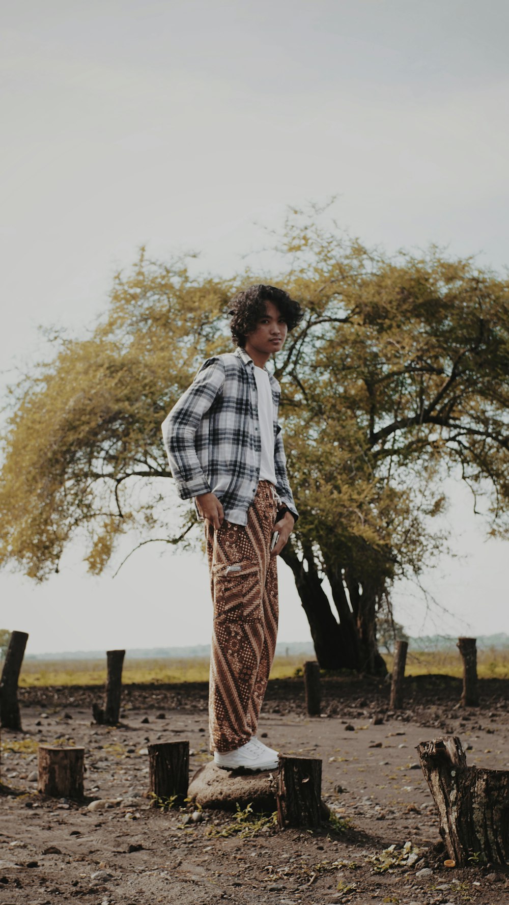 woman in white and black plaid dress shirt and brown skirt standing near trees during daytime