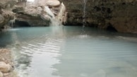 Peaceful natural spring water pool with stone edges and plants around.