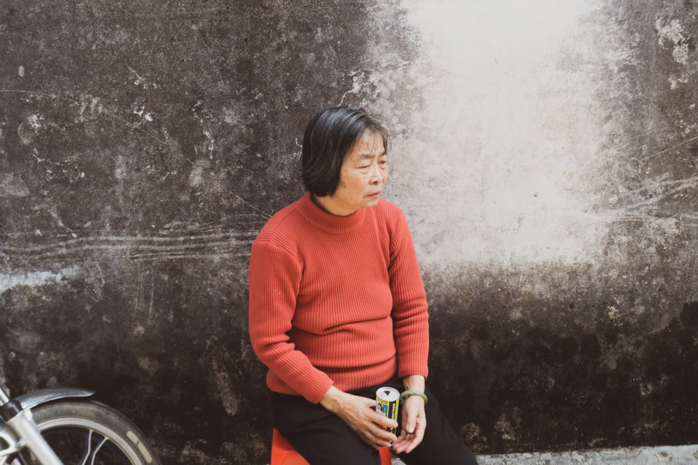 woman in orange sweater standing beside gray concrete wall