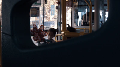 A cheerful child waving from inside a brightly colored Kabu electric bus, visible through large windows.