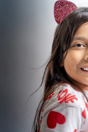 A child wearing a headband with sparkly red cat ears and a white shirt adorned with red hearts and the word 'love'. The composition captures a portion of the child's face, showcasing long brown hair and a cheerful expression.