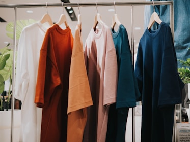 Several T-shirts in different colors are hanging on wooden hangers from a metal rod.