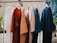 Several T-shirts in different colors are hanging on wooden hangers from a metal rod.