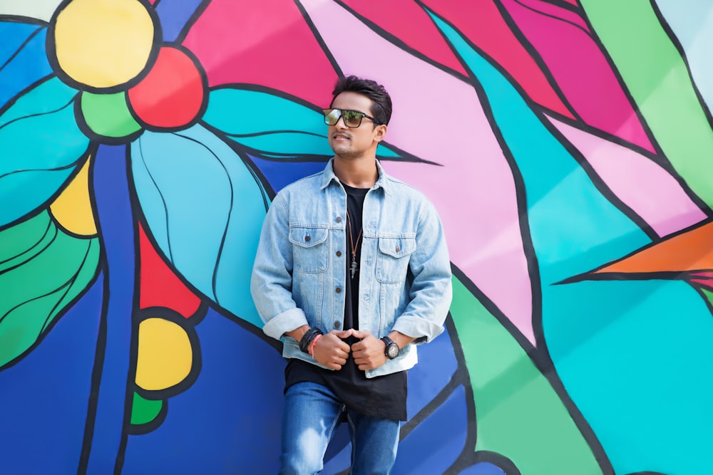 man in blue denim button up jacket standing beside wall with graffiti