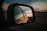 black car side mirror reflecting orange and white cloudy sky during daytime