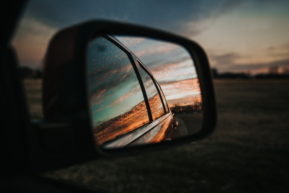 Specchietto retrovisore nero dell'auto che riflette il cielo nuvoloso arancione e bianco durante il giorno