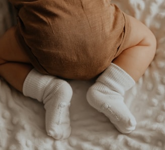 baby in white socks lying on bed
